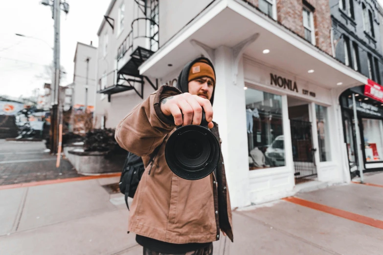 a man holding a camera in front of a building, by Niko Henrichon, pexels contest winner, pointing at the camera, photo for a store, carson ellis, video footage