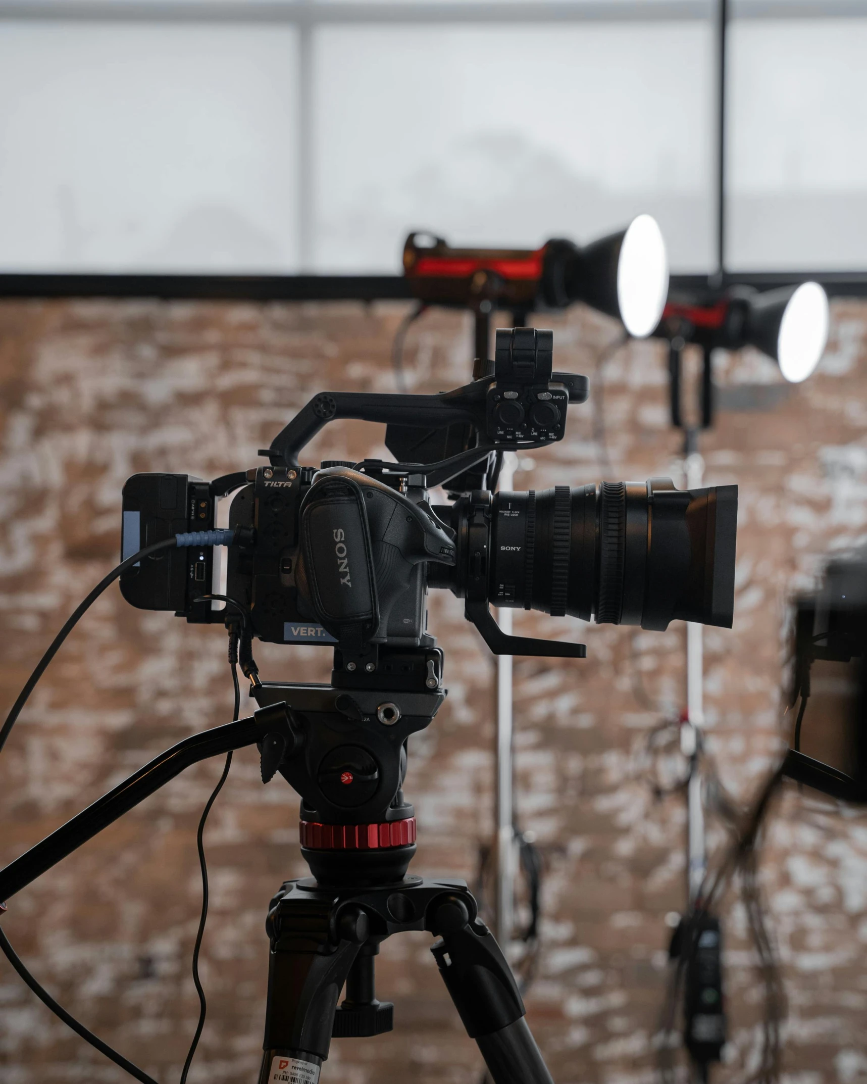 a camera sitting on top of a tripod in front of a brick wall, pexels contest winner, video art, cinema studio lights, red camera, standing microphones, footage of a theater stage