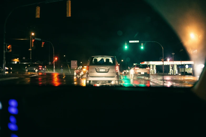 a car driving down a city street at night, a picture, unsplash contest winner, realism, street lights water refraction, intersection, people at night, dreary lighting