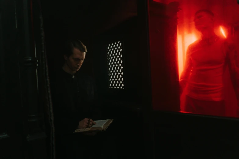 a man standing in front of a red light, renaissance, reading an evil demonic book, man looks out of a train window, priest, in a pitch black room