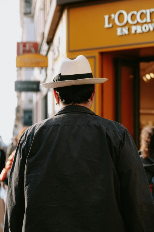 a man in a hat is walking down the street, trending on unsplash, renaissance, photograph of san francisco, back of head, wearing a fancy jacket, shops