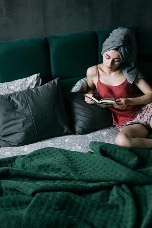 a woman sitting on a bed reading a book, dark green color scheme, fully functional, bedhead, chilling