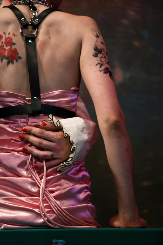 a woman in a pink dress with tattoos on her back, a tattoo, inspired by Nan Goldin, renaissance, brutalist fashion show, holding arms on holsters, embellishment, slide show