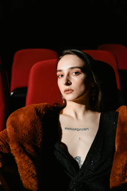 a woman sitting in a chair in a movie theater, an album cover, inspired by Elsa Bleda, trending on pexels, antipodeans, dilraba dilmurat, portrait androgynous girl, [ theatrical ], fur covering her chest