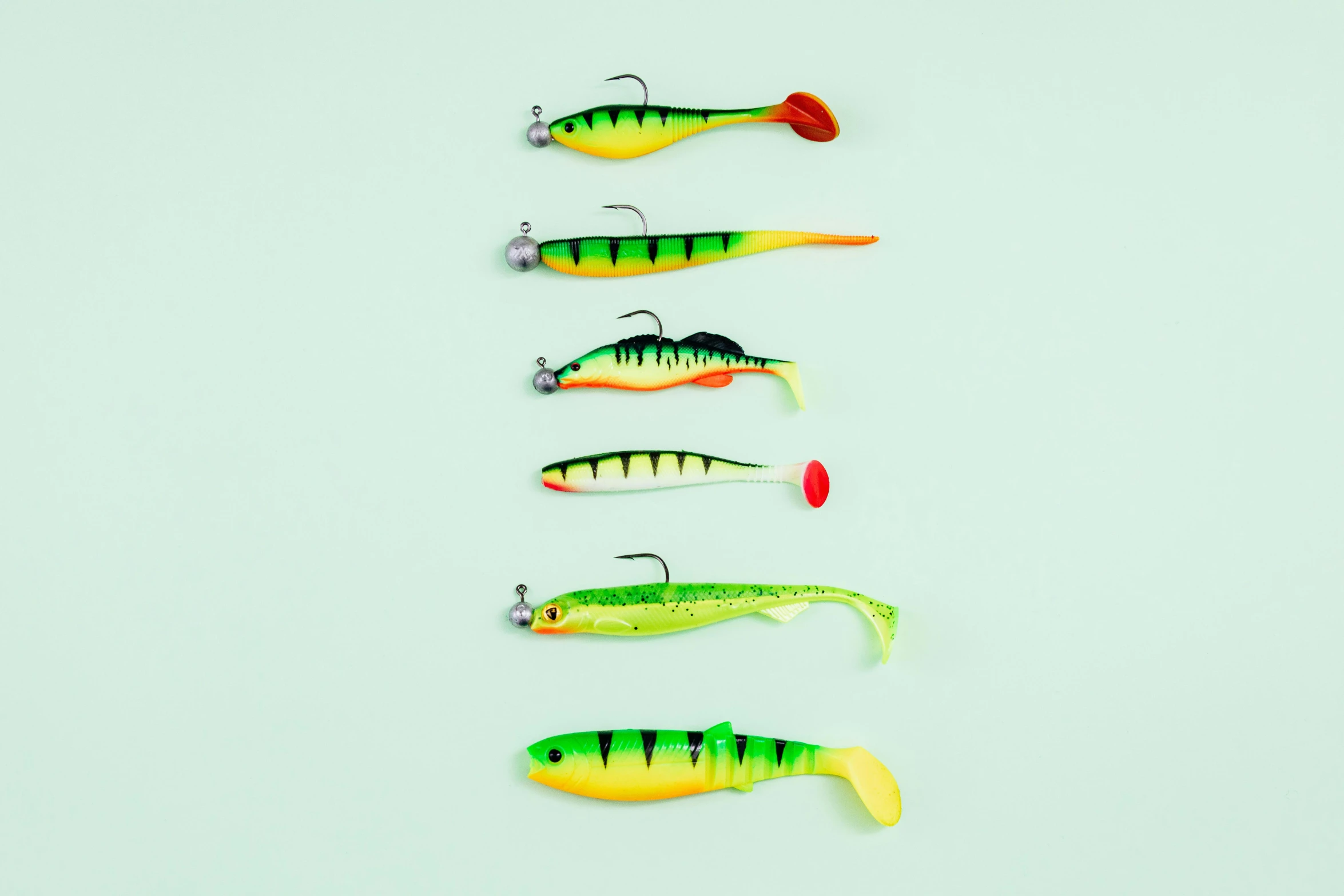 a number of fishing lures on a white surface, by Julia Pishtar, with tail, 6 pack, ice fish shape, on a bright day