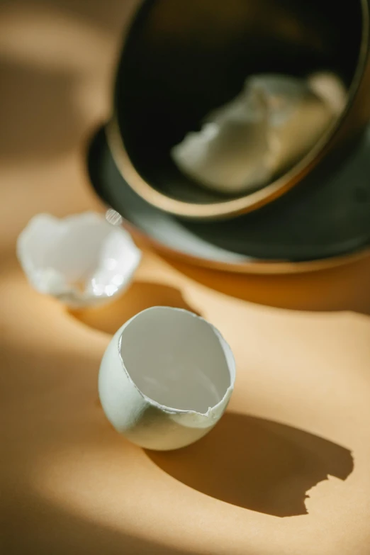 a broken egg sitting on top of a table next to a mirror, a still life, inspired by Ma Yuan, trending on unsplash, cups and balls, studio medium format photograph, low detail, made of silk paper