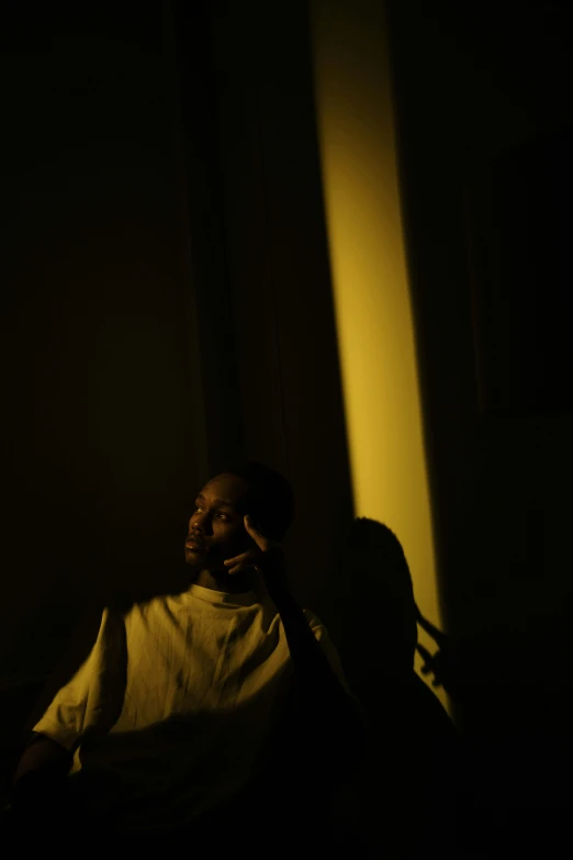 a man sitting in a chair talking on a cell phone, an album cover, inspired by Gordon Parks, unsplash, light and space, lowkey lighting, profile portrait, ignant, yellow light