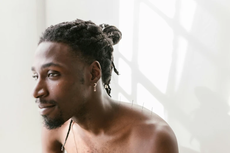 a shirtless man sitting in front of a laptop computer, a photo, inspired by Barthélemy Menn, trending on pexels, black arts movement, short dreadlocks with beads, hair styled in a bun, on a pale background, playboi carti portrait