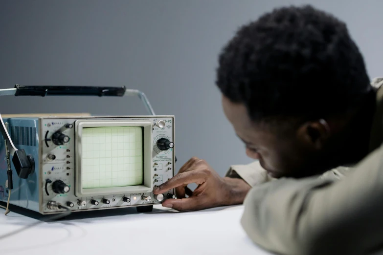 a man sitting at a table with a radio in front of him, unsplash, computer art, oscilloscope, afro tech, scientific equipment, teaching