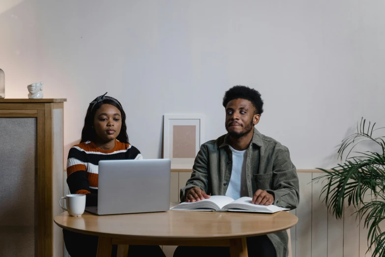 a man and a woman sitting at a table with a laptop, by Carey Morris, trending on pexels, renaissance, ( ( dark skin ) ), studious, looking serious, slightly minimal