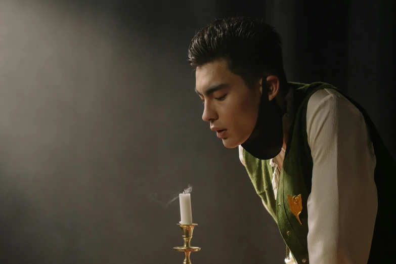 a man sitting at a table with a lit candle, an album cover, inspired by Ding Guanpeng, romanticism, the actor, behind the scenes photo, [ theatrical ], darren quach
