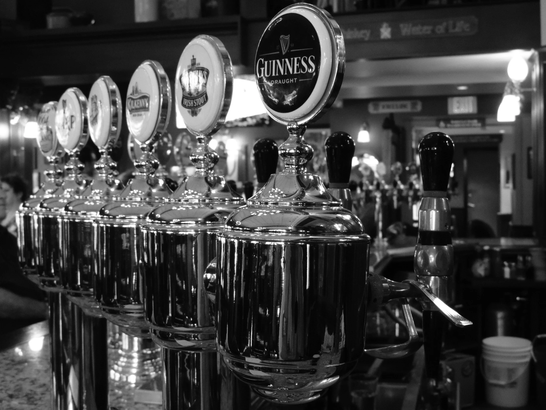 a row of beer taps sitting on top of a bar, by Matt Stewart, 4k greyscale hd photography, ireland, facebook photo, shiny!!