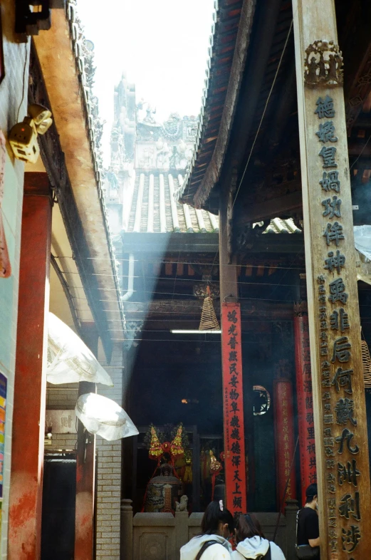 a group of people standing in front of a building, a silk screen, inspired by Wen Zhengming, unsplash, light and space, peaked wooden roofs, holy light rays, old shops, guanyin of the southern seas