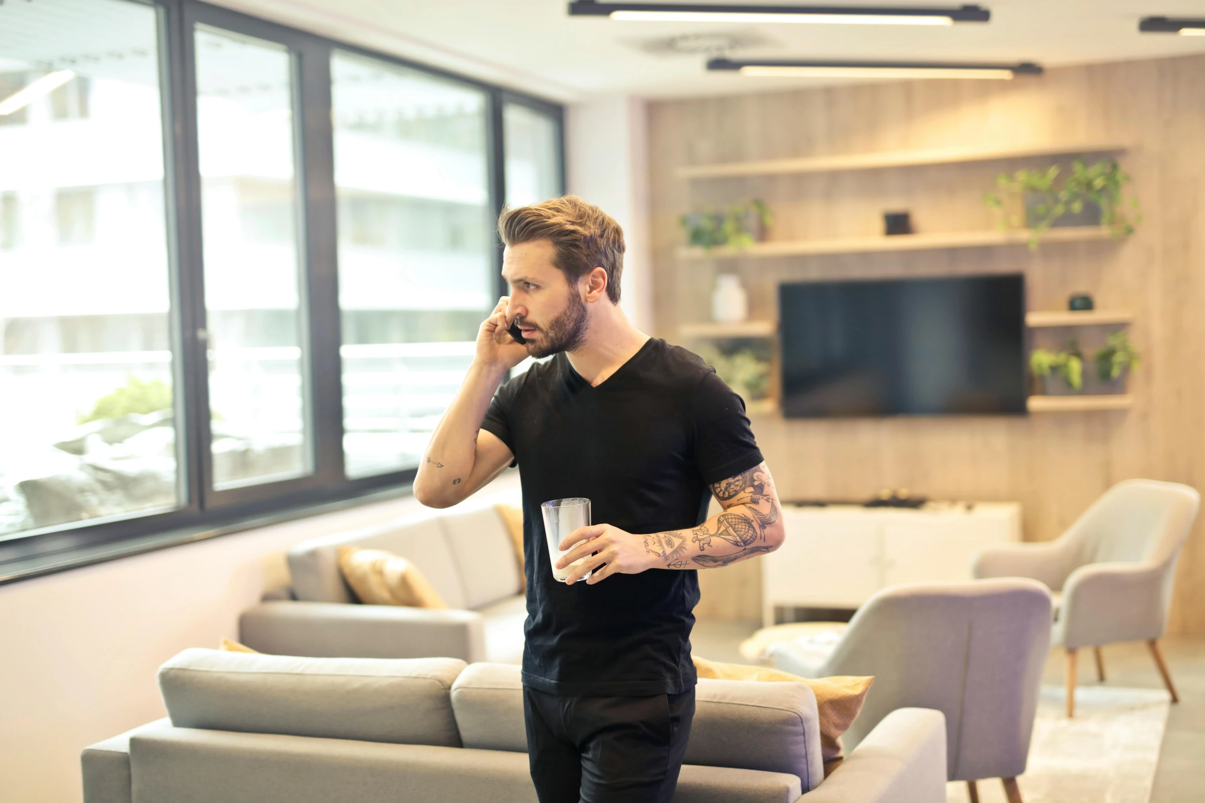 a man standing in a living room talking on a cell phone, trending on pexels, tattooed man, office clothes, open plan, actor