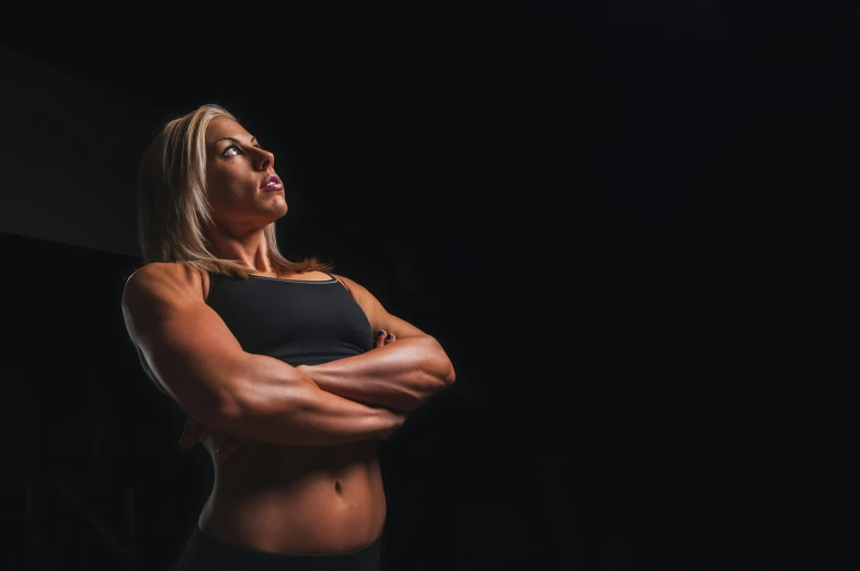 a woman standing in the dark with her arms crossed, by Adam Marczyński, body builder, profile image