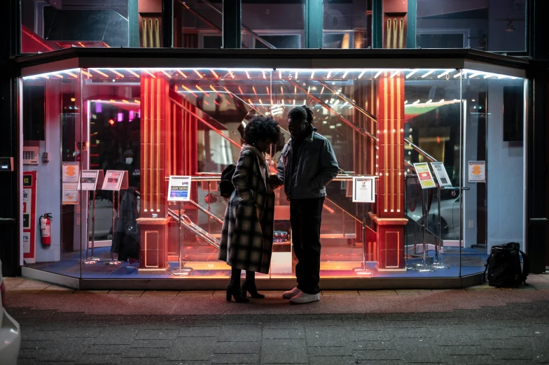 a couple of people standing in front of a store, by Lee Loughridge, pexels contest winner, cold neon lighting, jukebox, private moment, palatial scene