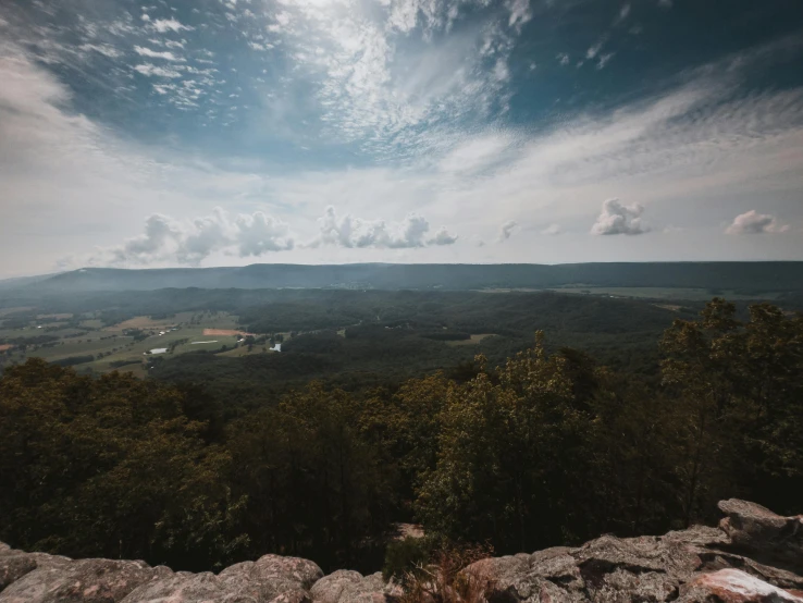 a view of a valley from the top of a mountain, by Robert Storm Petersen, unsplash contest winner, visual art, william penn state forest, partly cloudy sky, high cliff, slightly pixelated