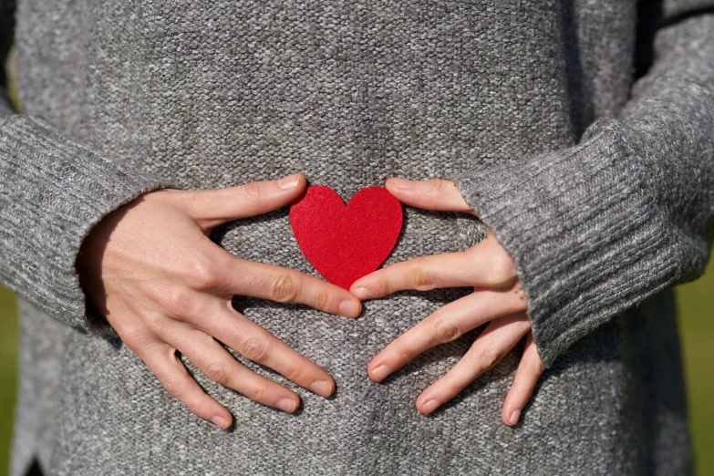 a woman holding a red heart in her hands, by Julia Pishtar, pexels, red sweater and gray pants, folds of belly flab, man with a blue heart, third trimester