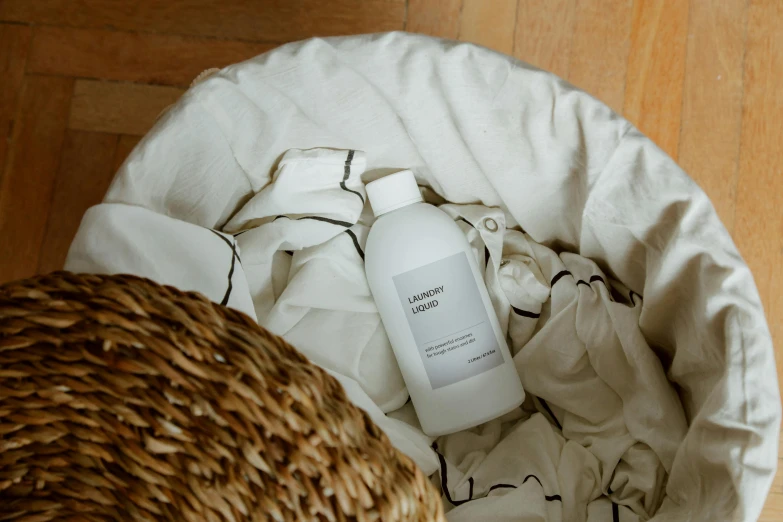 a bottle of lotion sitting in a basket on the floor, unsplash contest winner, white splendid fabric, in a laundry mat, clean and pristine design, ignant