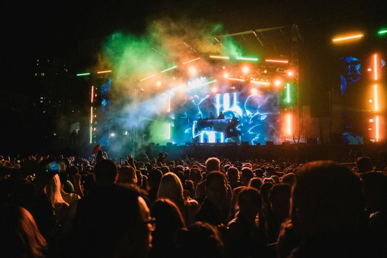 a group of people that are standing in front of a stage, festival vibes, glowing epicentre, electric sky, shot from the side