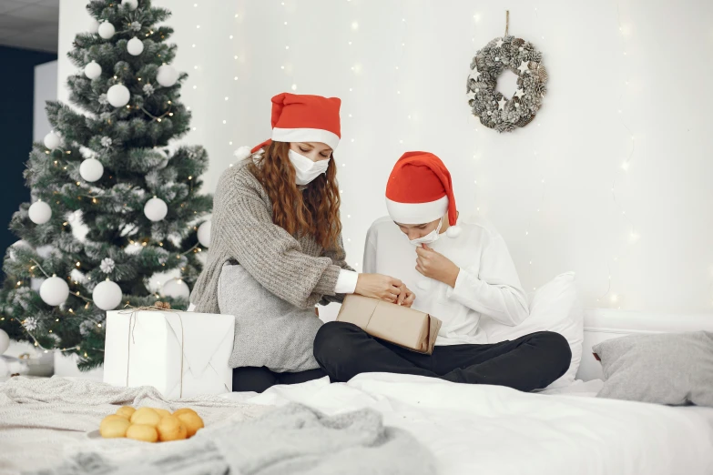 a couple of women sitting on top of a bed next to a christmas tree, pexels, masked doctors, grey, presents, wearing bandit mask
