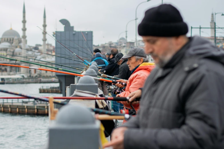 a group of people standing next to a body of water, istanbul, fishing, in a row, people watching