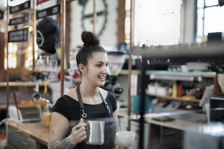 a woman standing in a kitchen holding a cup, by Lee Loughridge, trending on unsplash, aussie baristas, female blacksmith, at the counter, tattooed