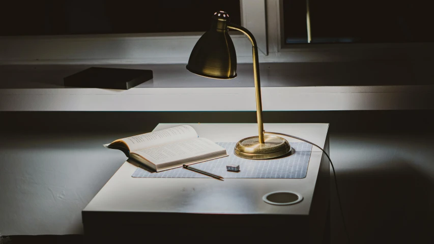 a lamp sitting on top of a table next to a book, unsplash contest winner, hyperrealism, desk, dusty library, cinematic counter light, instagram post