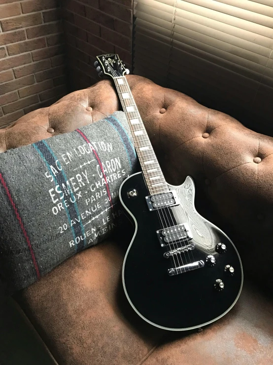 a guitar sitting on top of a couch next to a pillow, gun metal grey, band merchandise, rich moody colour, very handsome