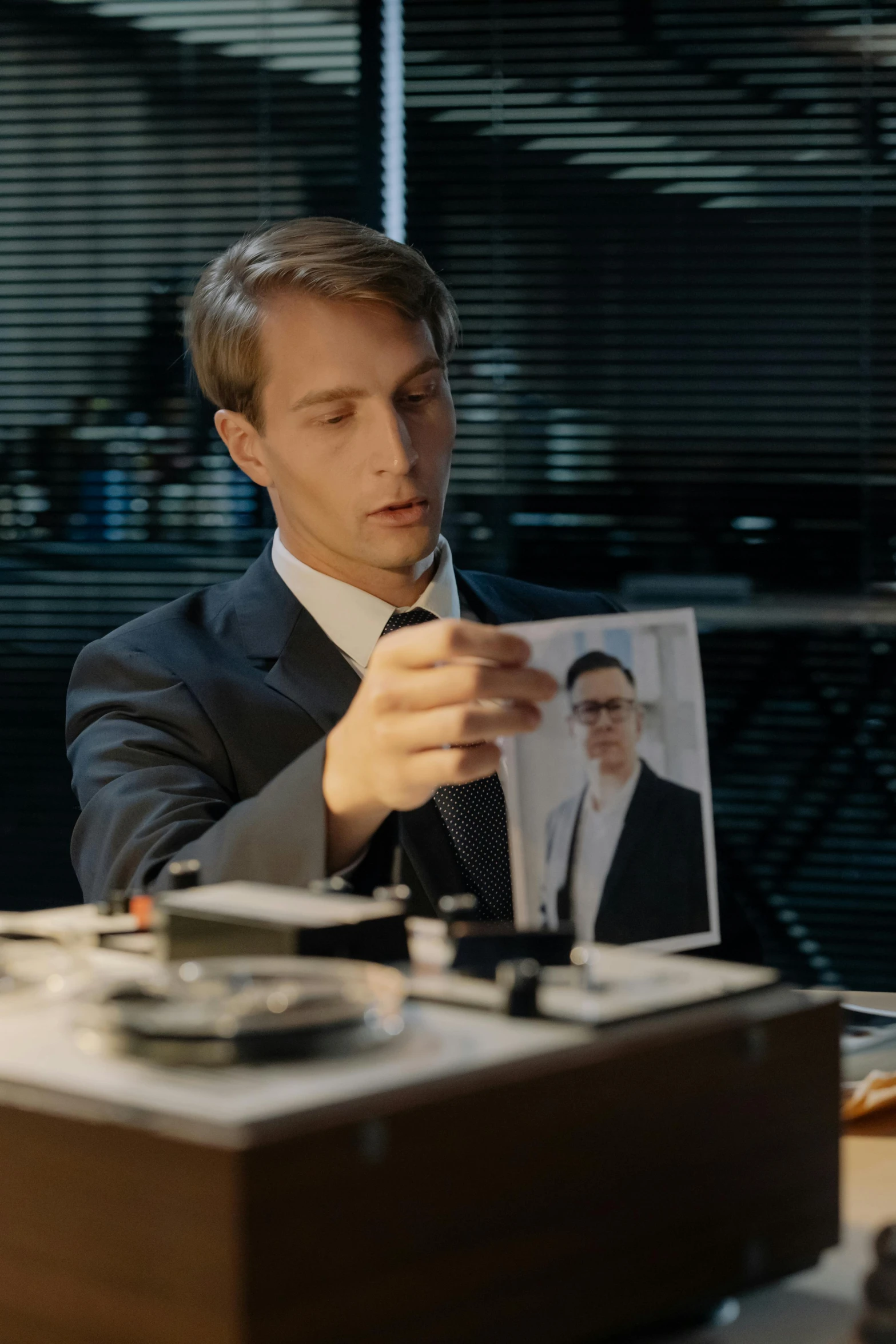 a man in a suit holding a picture of himself, a picture, inspired by Oskar Lüthy, trending on reddit, in a movie still cinematic, live-action archival footage, caspar david, on a desk