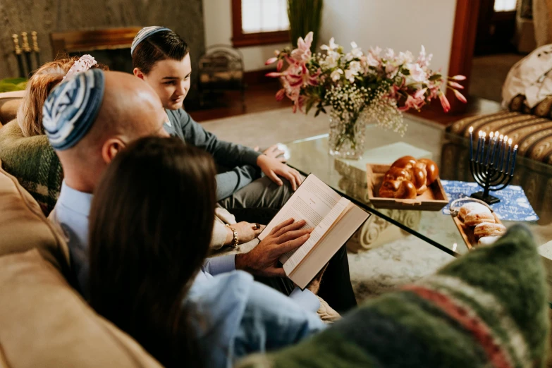 a man and woman sitting on a couch reading a book, by Carey Morris, pexels contest winner, holy ceremony, group sit at table, teenage boy, funeral