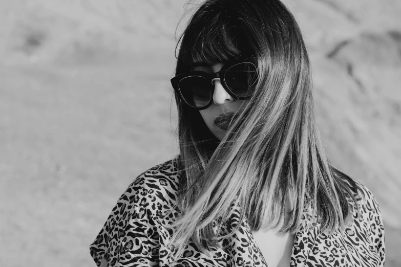 a black and white photo of a woman wearing sunglasses, a black and white photo, pexels, purism, brown long hair with bangs, patterned clothing, portrait featured on unsplash, wild hairs