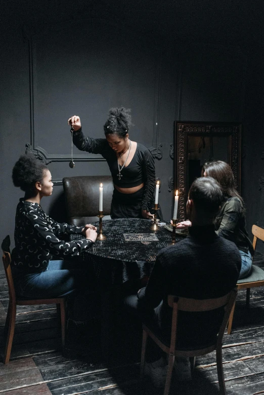 a group of people sitting around a table, an album cover, by Elsa Bleda, pexels contest winner, renaissance, casting an evil spell, harmony black room, female occultist, promotional image