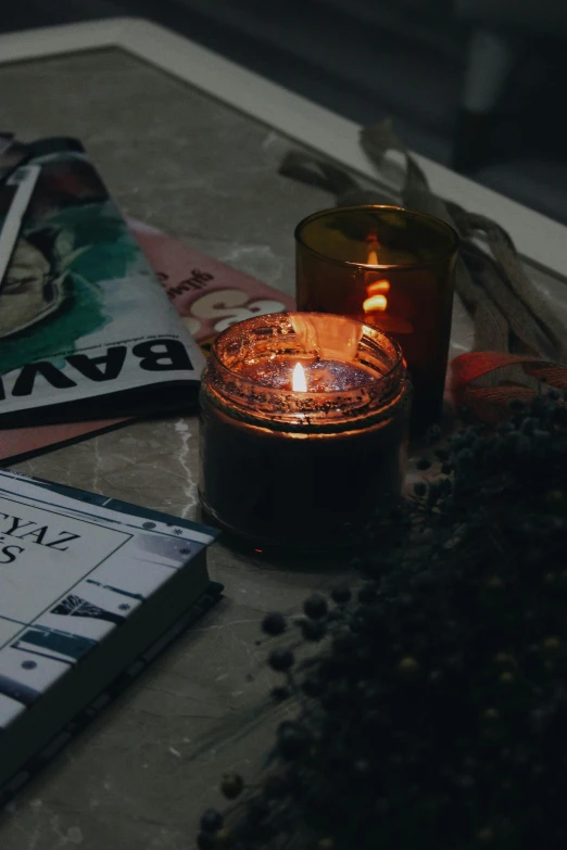 a candle sitting on top of a table next to a book, profile image, mixed materials, dark hues, a high angle shot