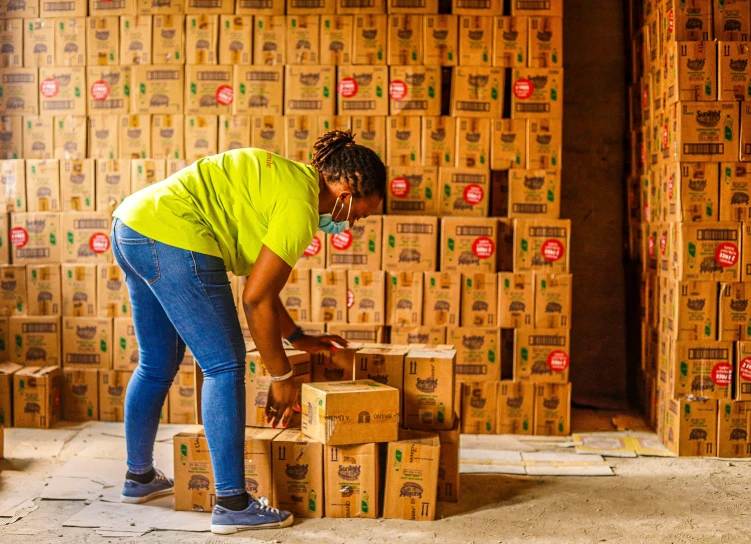 a woman standing next to a pile of boxes, process art, jamaica, inspect in inventory image, thumbnail, cooking oil