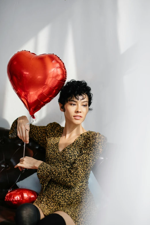 a woman sitting on a couch holding a heart shaped balloon, with black hair, ashteroth, official store photo, falling hearts