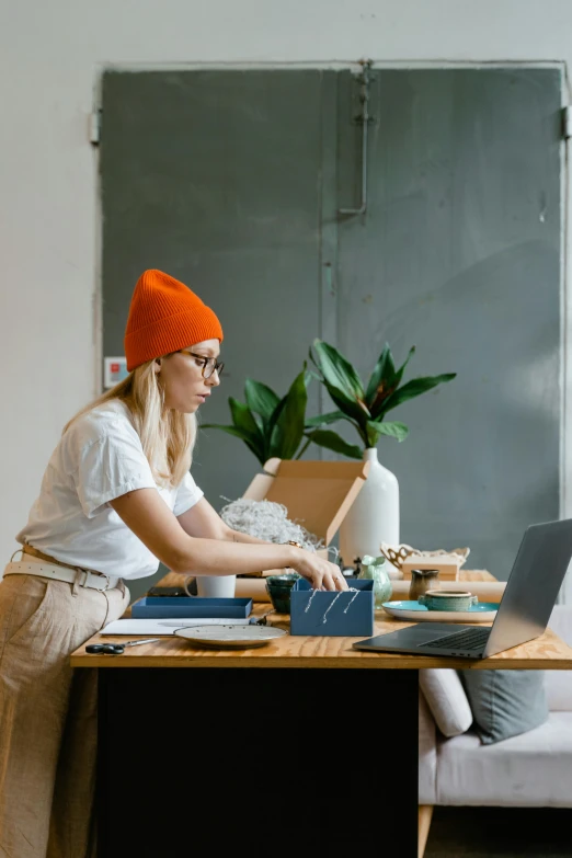 a woman sitting at a table working on a laptop, trending on pexels, arbeitsrat für kunst, woman with hat, inspect in inventory image, 9 9 designs, casually dressed