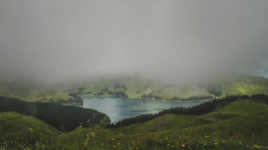 a large body of water sitting on top of a lush green hillside, by Daniel Lieske, pexels contest winner, hurufiyya, under a gray foggy sky, endless lake, te pae, comforting and familiar