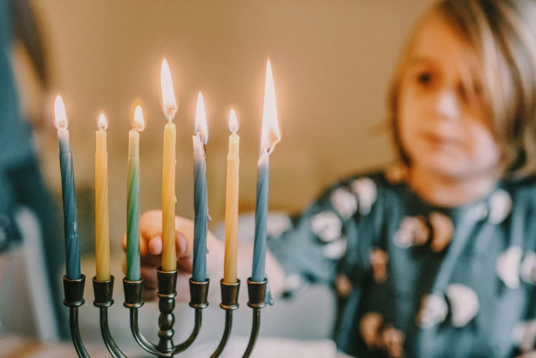 a little girl sitting at a table with a menorah, trending on unsplash, wearing festive clothing, light over boy, colourised, candle