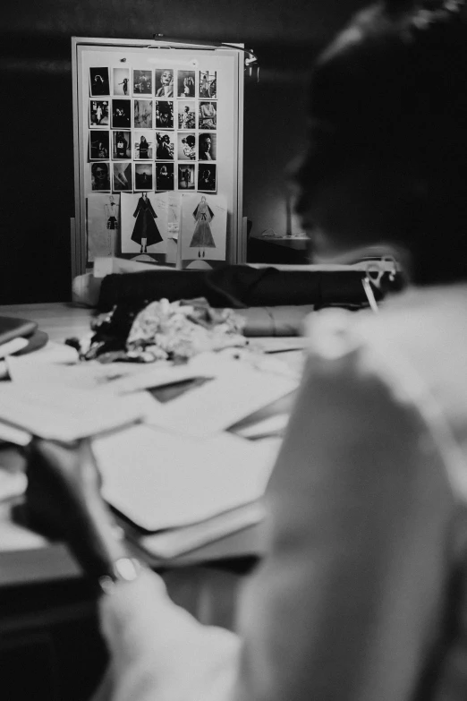 a black and white photo of a woman sitting at a table, unsplash, process art, character sheets on table, theater dressing room, dress and cloth, moodboard
