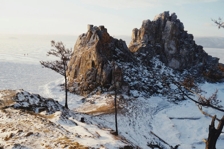 a man standing on top of a snow covered mountain, a detailed matte painting, inspired by Konstantin Vasilyev, unsplash contest winner, near lake baikal, tall big rocks, beautiful composition 3 - d 4 k, ultrawide lens”