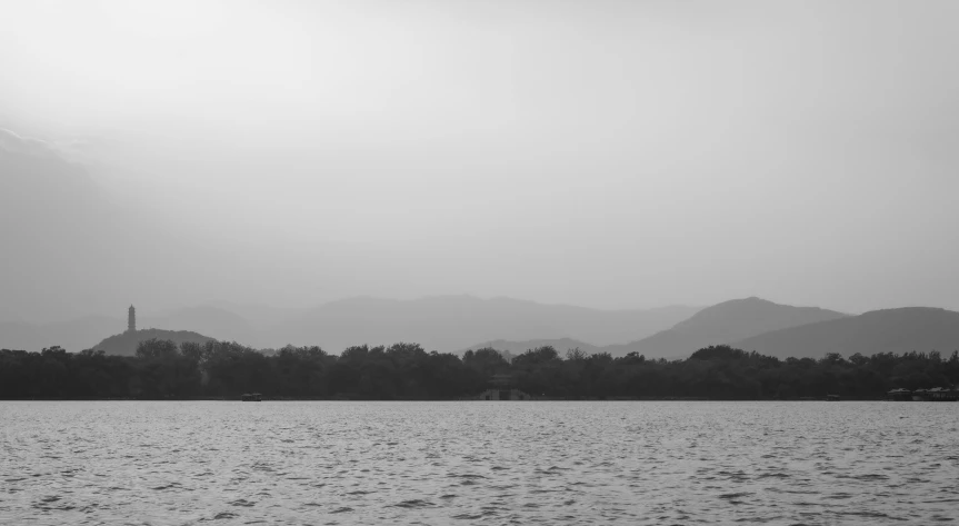 a black and white photo of a body of water, by Saurabh Jethani, pexels contest winner, minimalism, hazy atmosphere, hills in the background, low quality footage, guwahati