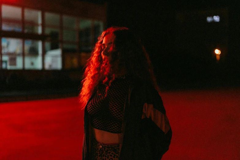 a woman standing in the middle of a street at night, an album cover, inspired by Elsa Bleda, pexels contest winner, renaissance, red curly hair, red neon light, red waist-long hair, official music video