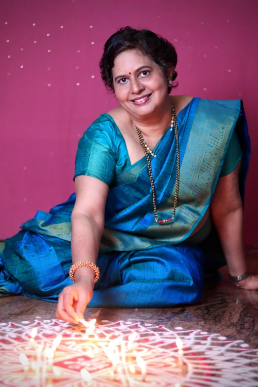 a woman sitting on the floor lighting a diya, inspired by T. K. Padmini, portrait image, lgbtq, recital, 2022 photograph