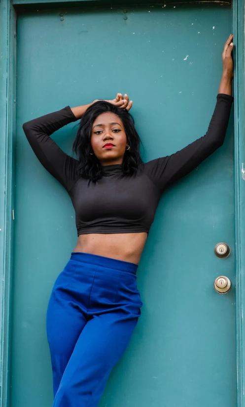 a woman leaning against a green door, an album cover, by Lily Delissa Joseph, trending on unsplash, happening, blue pants, crop shirt and strong abs, 15081959 21121991 01012000 4k, black teenage girl