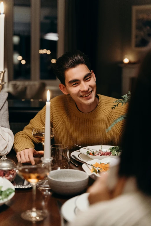 a group of people sitting around a dinner table, he is wearing a brown sweater, happy friend, candle lit, photo of a model