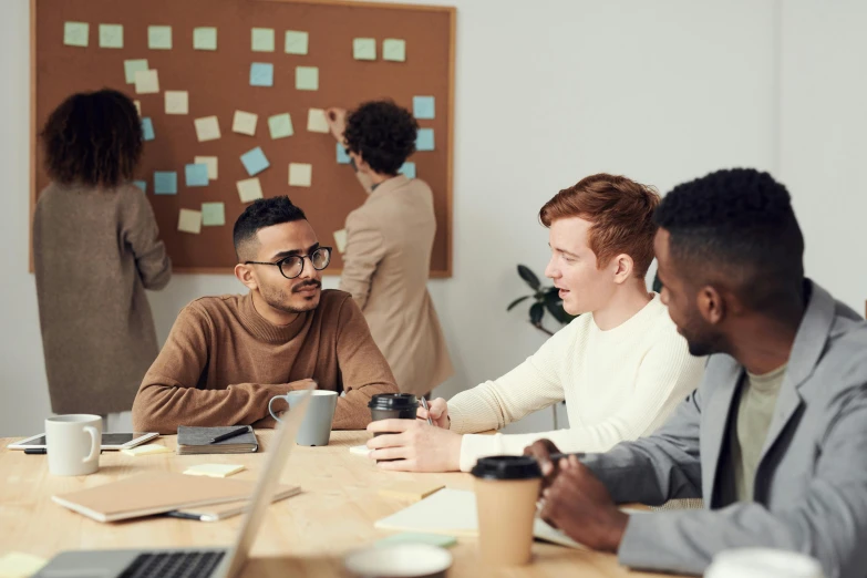 a group of people sitting around a wooden table, trending on pexels, whiteboards, lachlan bailey, sitting on a mocha-colored table, competition winning