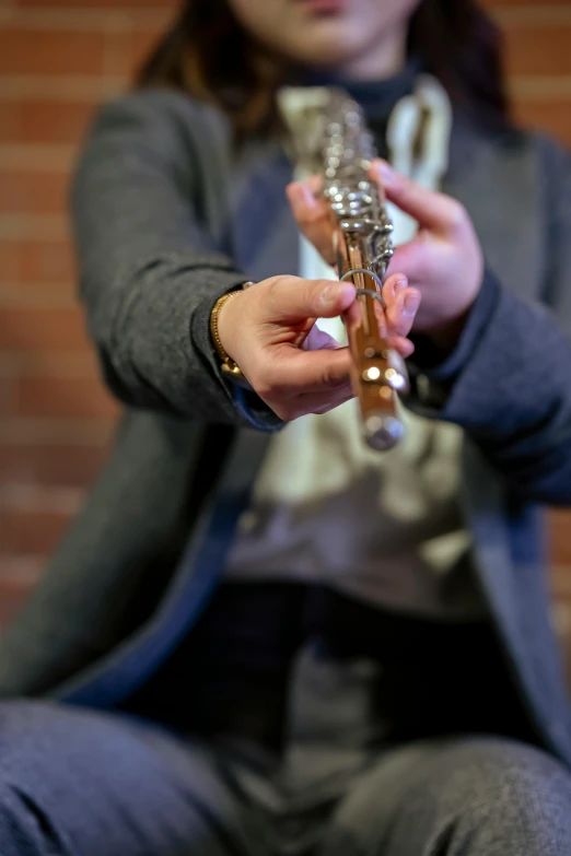 a woman sitting in front of a brick wall holding a microphone, by Nina Hamnett, unsplash, hand holding medieval sword, instrument, high angle close up shot, multiple stories