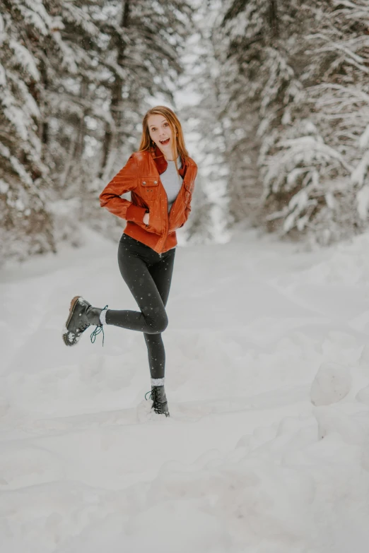 a woman in an orange jacket is running through the snow, a portrait, pexels contest winner, leather boots, avatar image, cute pose, ( redhead