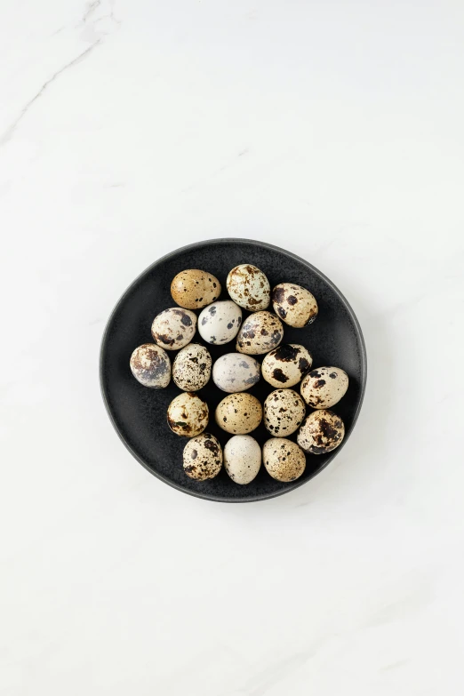quails in a black bowl on a white table, an illustration of, by Ben Zoeller, unsplash, baroque, dragon eggs, white with chocolate brown spots, 1 6 x 1 6, high angle shot